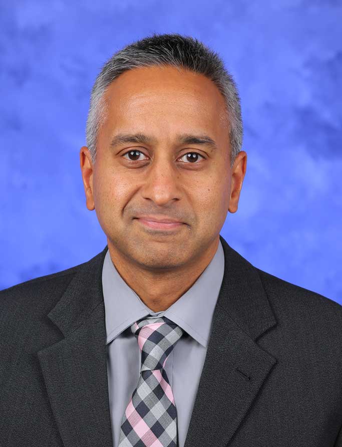 Jay Raman, MD, is the Chair of Urology. He is pictured in a white medical coat against a blue background. 